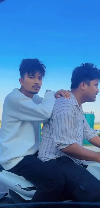 Two friends riding a motorbike under clear blue skies.