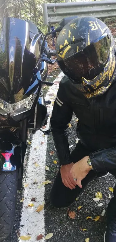 Biker in black leather crouching beside motorcycle on forest road.