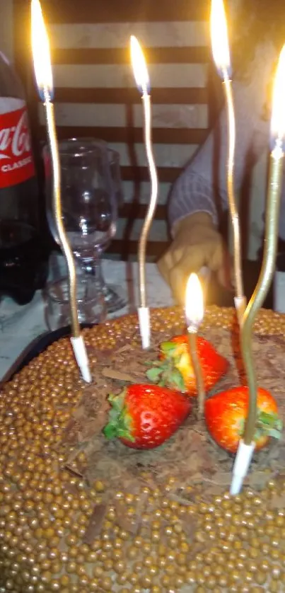 Chocolate birthday cake with candles lit, decorated with strawberries.