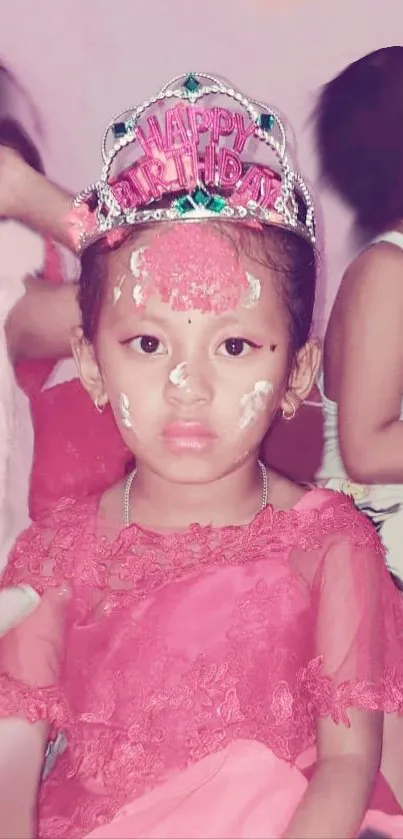 Young girl in pink dress with birthday crown and cake on face.