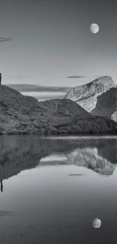 Monochrome landscape with moon above mountains reflected in water.