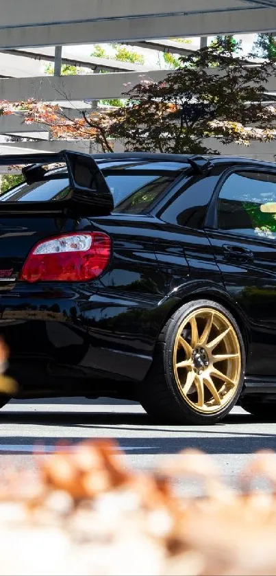 Black sports car with golden wheels under carport.