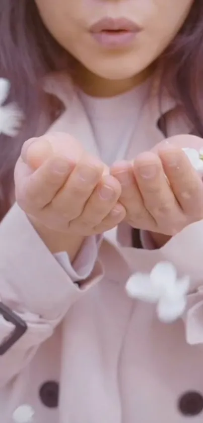 Woman blowing flower petals in pink coat.