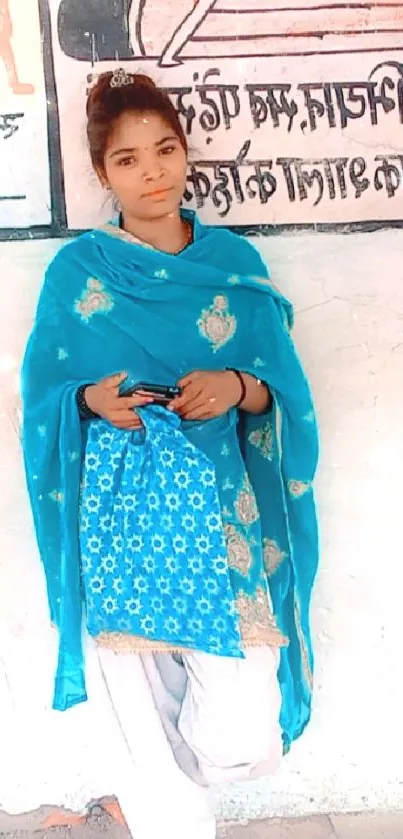 Woman in blue ethnic attire against mural background.