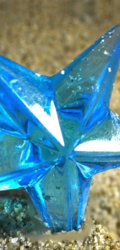 Blue glass star resting on sandy surface wallpaper.