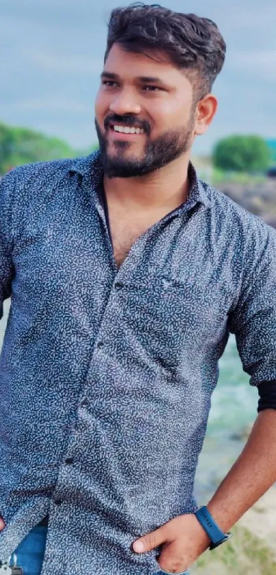 Smiling man in a blue shirt outdoors with a natural background.