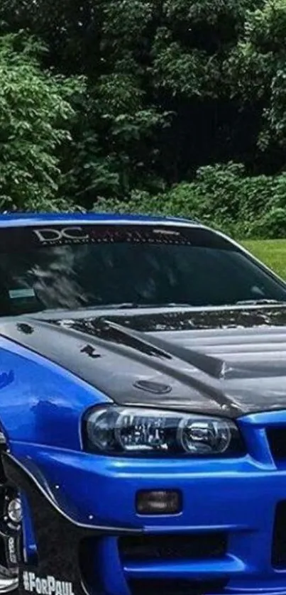 Blue sports car parked in front of a lush green forest, showcasing elegance.