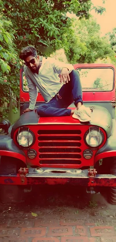 Person sitting on a vintage red jeep in a lush outdoor setting.