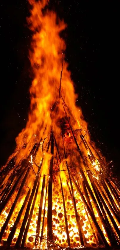 Vibrant bonfire blaze with fiery flames and wooden structure at night.