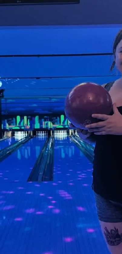 Smiling person holding bowling ball in neon-lit alley.