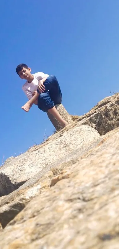 Boy sitting on a rocky cliff under a clear blue sky.