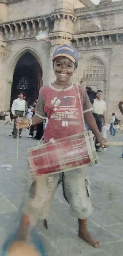 Boy playing drum in front of historic architectural structure.