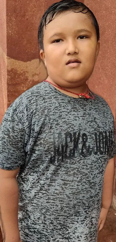 A young boy in a gray t-shirt stands against a red wall.