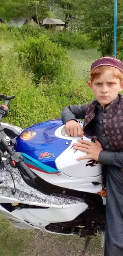 Young boy in traditional attire with motorbike in scenic countryside.