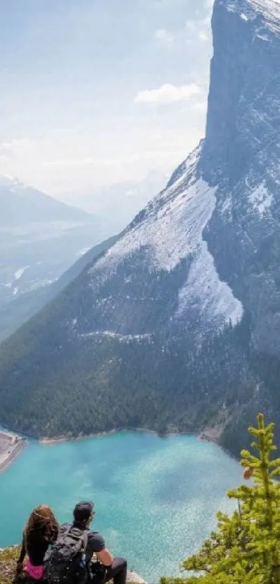 Hikers admire a stunning mountain and lake view in this mobile wallpaper.