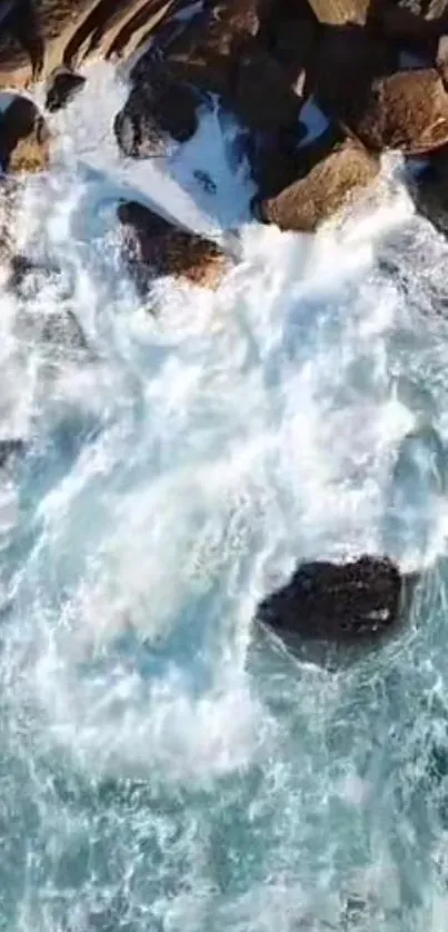 Aerial view of ocean waves crashing onto rocks with a stunning blue tone.