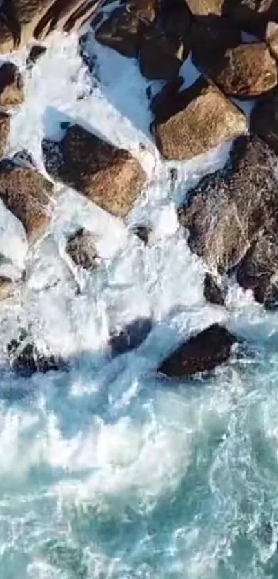 Aerial view of ocean waves crashing against rocks on a sandy shore.