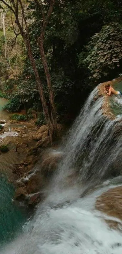 Person sitting above a stunning waterfall in the heart of a lush forest scenery.