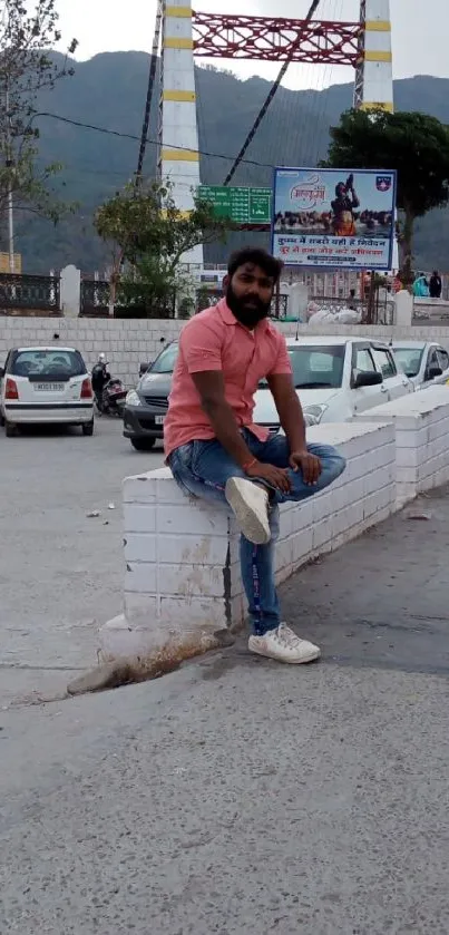 Man sitting on wall with bridge and city backdrop.