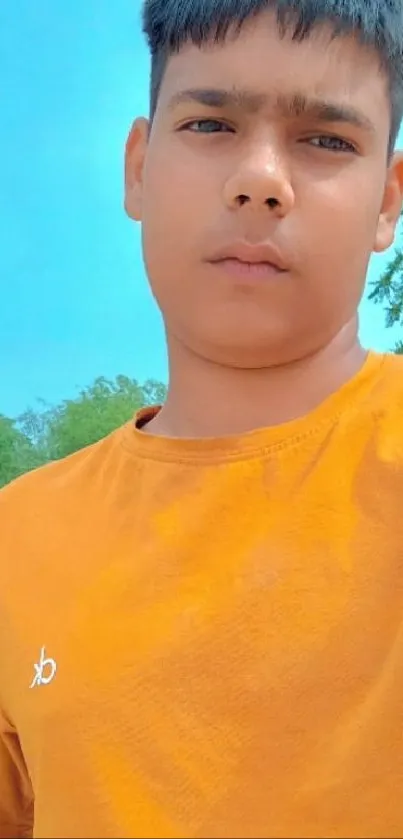 Person in orange shirt under a blue sky, showing casual summer fashion.