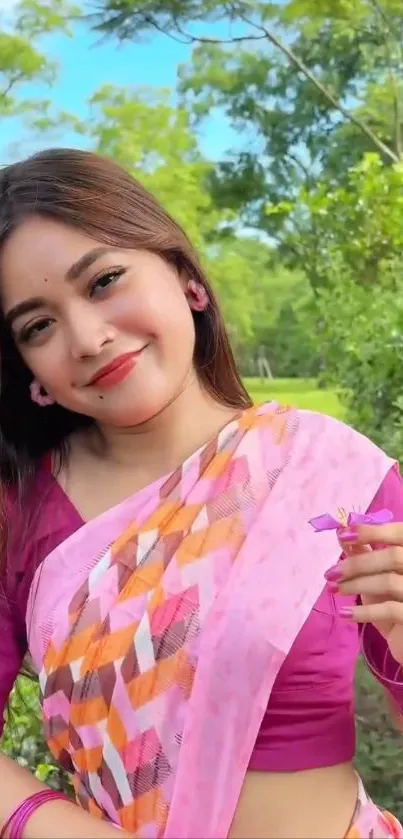 Smiling woman in colorful sari holding a flower outdoors.