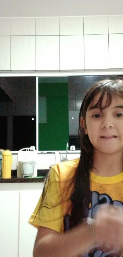 Child in a bright kitchen wearing a yellow shirt.