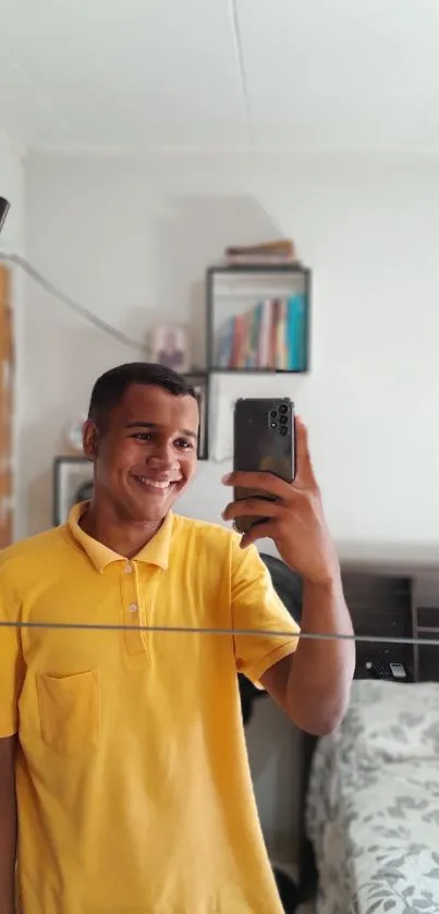 Mirror selfie of a smiling individual in a yellow shirt in a bright room.