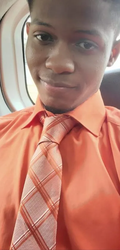 Man in an orange shirt and tie smiling while seated indoors.