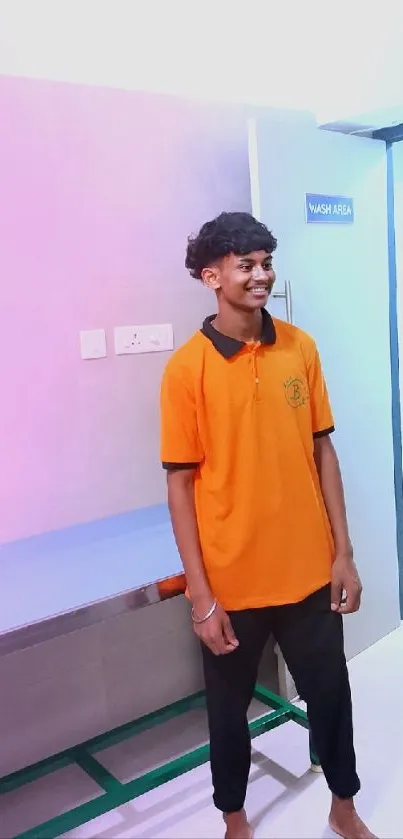 Young man in orange shirt in a pastel-lit modern room.