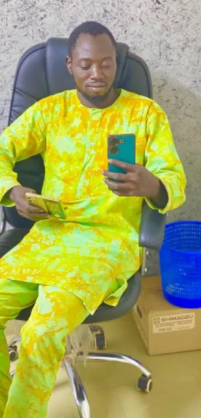 Person in bright yellow outfit holding a smartphone, seated in an office chair.