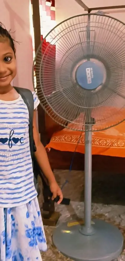 Child smiling beside a standing fan in a cozy room.