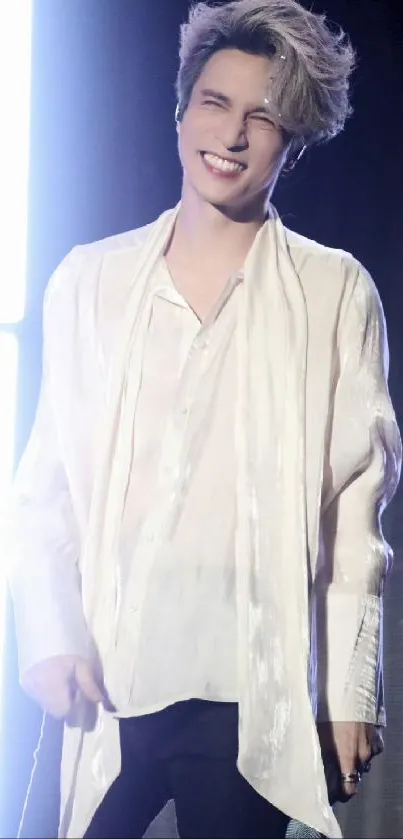 A joyful man in a white shirt, smiling brightly on stage.