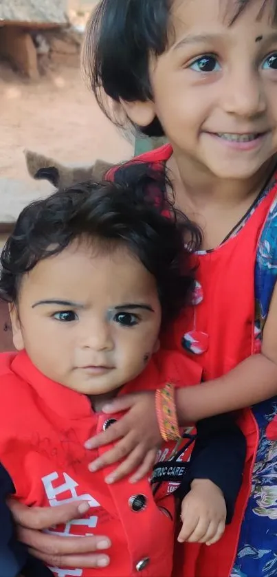 Two smiling children in colorful red outfits with a joyful expression.