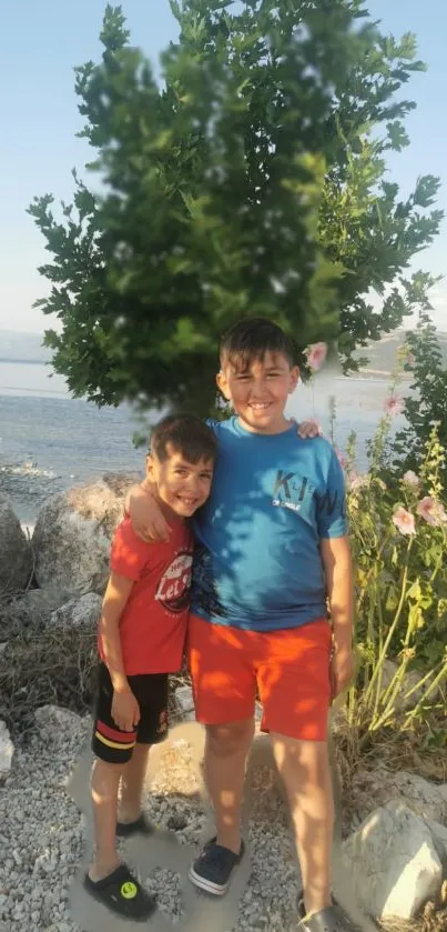 Two young brothers smiling near the seaside with trees and flowers.