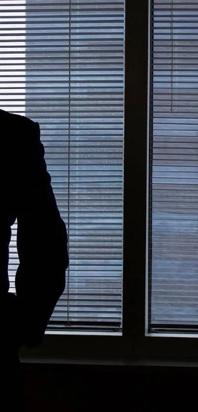 Silhouette of a person looking out an office window with blinds.