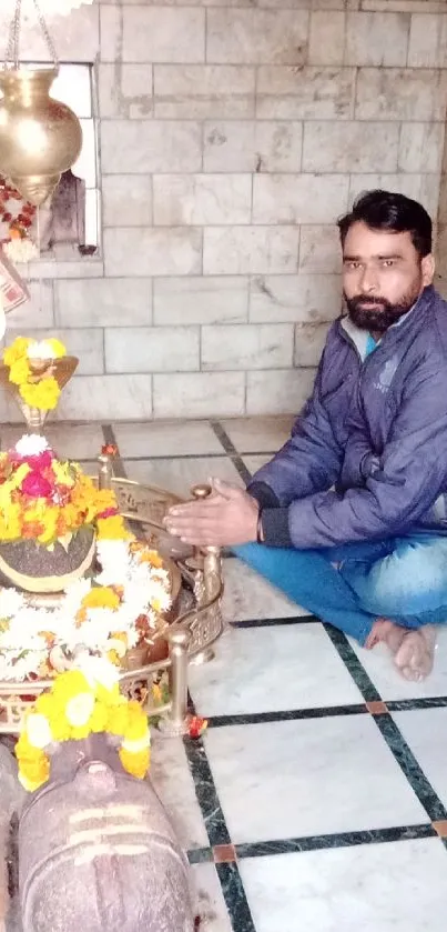 Person meditating in a temple surrounded by colorful flowers and sacred items.