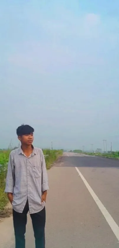 A man stands by a quiet roadside under a clear sky.