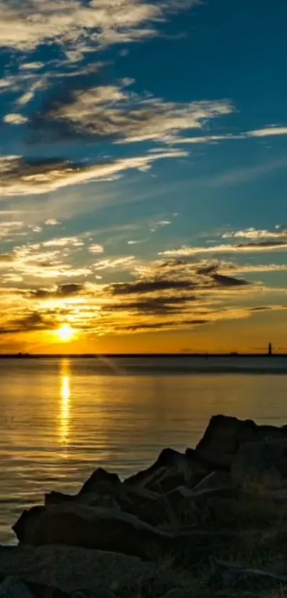 Sunset over ocean with rocks and cloudy sky.