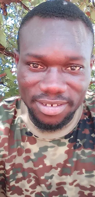 Man in camo shirt against leafy background.