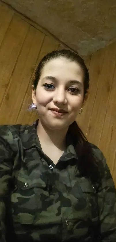 Person in camouflage shirt with a wooden background.