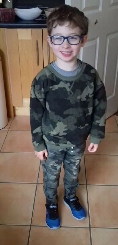 Child in a camouflage outfit standing indoors with a smile.