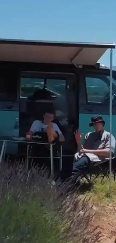 Two people relax in front of their camper van under a sunny blue sky.