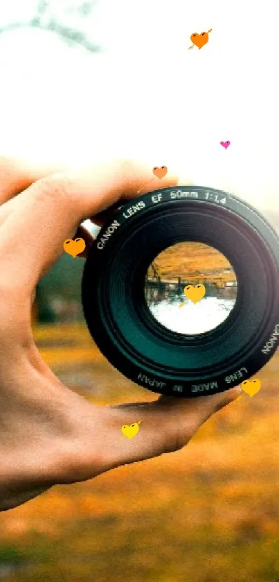 Hand holding a camera lens against a nature backdrop.