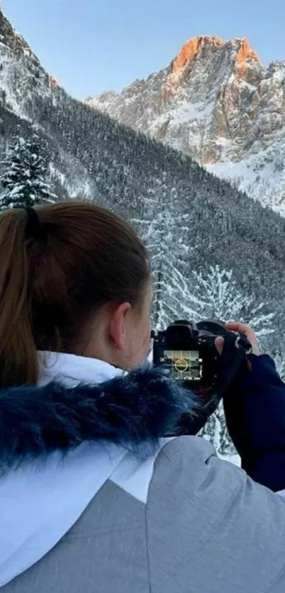 Photographer capturing snowy mountain scene at sunrise.