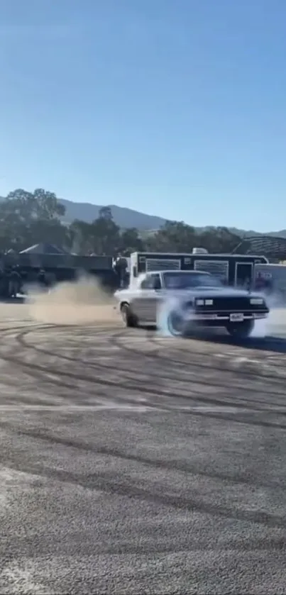 Classic car drifts on pavement with mountains and blue sky.