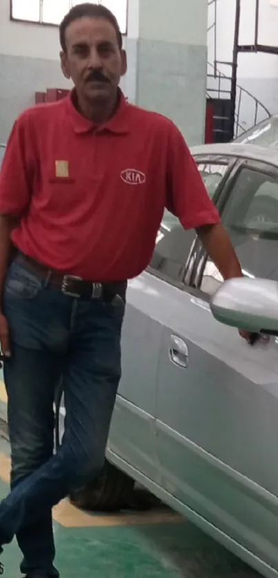 Man in a red shirt standing by a car in a workshop.