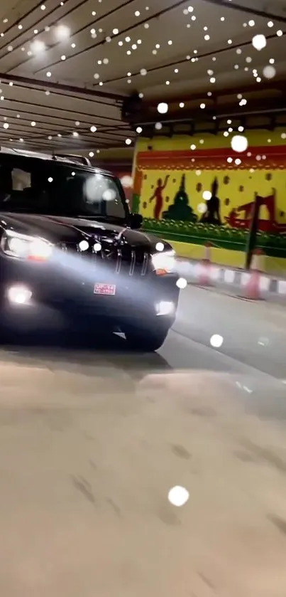 Black car driving through graffiti-decorated tunnel at night.