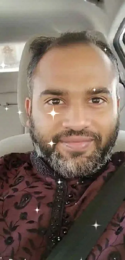 Man in car wearing maroon shirt, smiling.