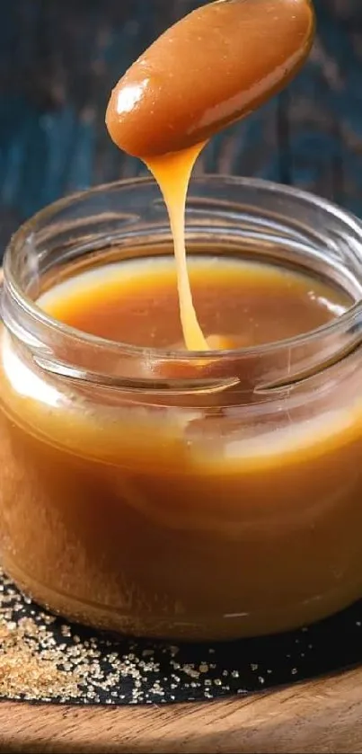 Caramel sauce dripping from spoon into jar on wooden tray.