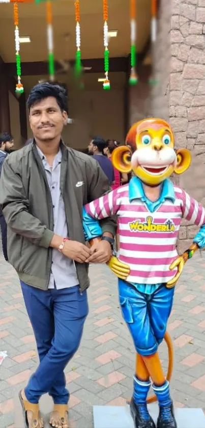 Man standing beside cartoon monkey statue with colorful background.